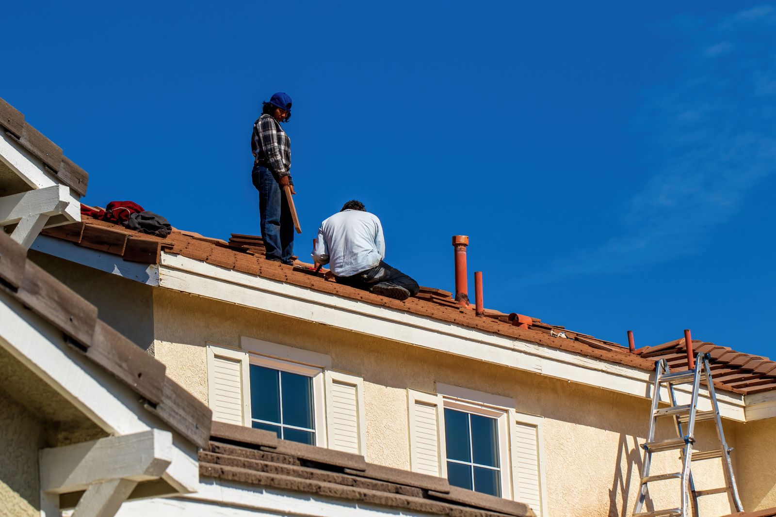 Builders repairing a clay tiled roof against a blue sky