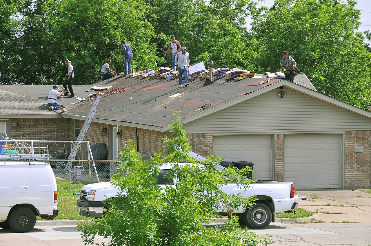 Crew replacing shingles across a suburban home roof